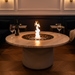 EcoSmart Round 20 Fire Pit Kit in a luxurious living room, featuring a circular design with a flame rising from black stones, surrounded by sophisticated furniture and wine glasses.