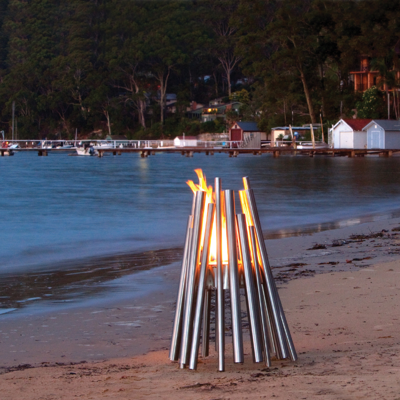 EcoSmart Stix Fire Pit on beachfront sand with glowing flame at dusk