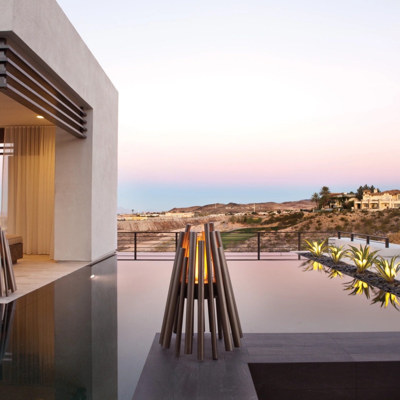EcoSmart Stix fire pits lit beside an infinity pool on a modern home terrace at dusk.