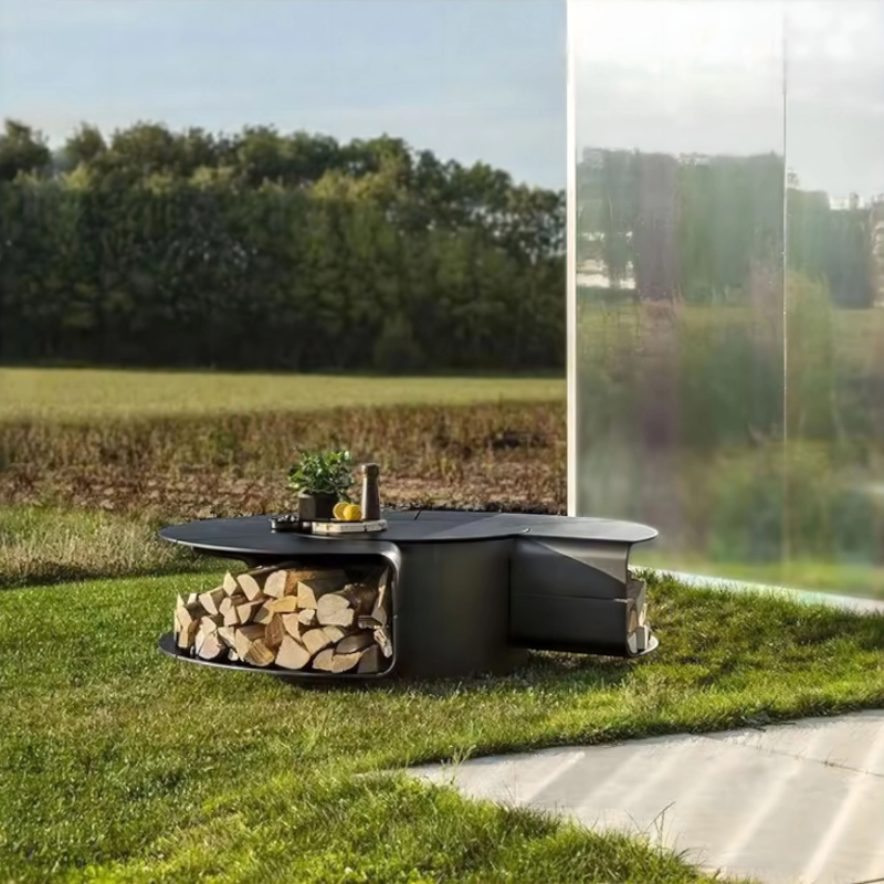 Low-profile Fabrizio Fire Pit styled as a sculptural outdoor fire pit table, shown on a lawn beside a reflective wall with integrated firewood storage and tabletop surface.