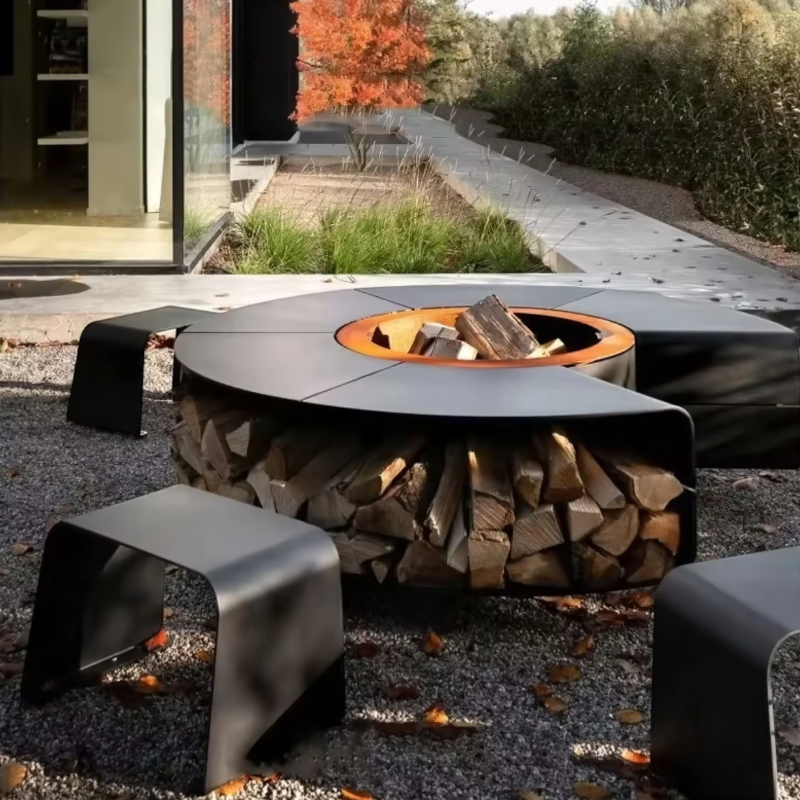 Fabrizio Fire Pit set in a landscaped outdoor garden with matching stools, featuring a circular fire pit table, central fire bowl, and integrated firewood storage beneath.