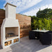 Close-up view of the Ochre Living Hotham Complete Fireplace Kit in a brick courtyard patio with stacked firewood, outdoor seating, and active fire, showing a practical outdoor fireplace installation in Australia.