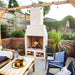 Ochre Living Hotham Complete Fireplace Kit with a large fire burning in a backyard patio setting with pergola lighting, lounge furniture, and stacked logs below, showing outdoor fireplace kits Australia in use.
