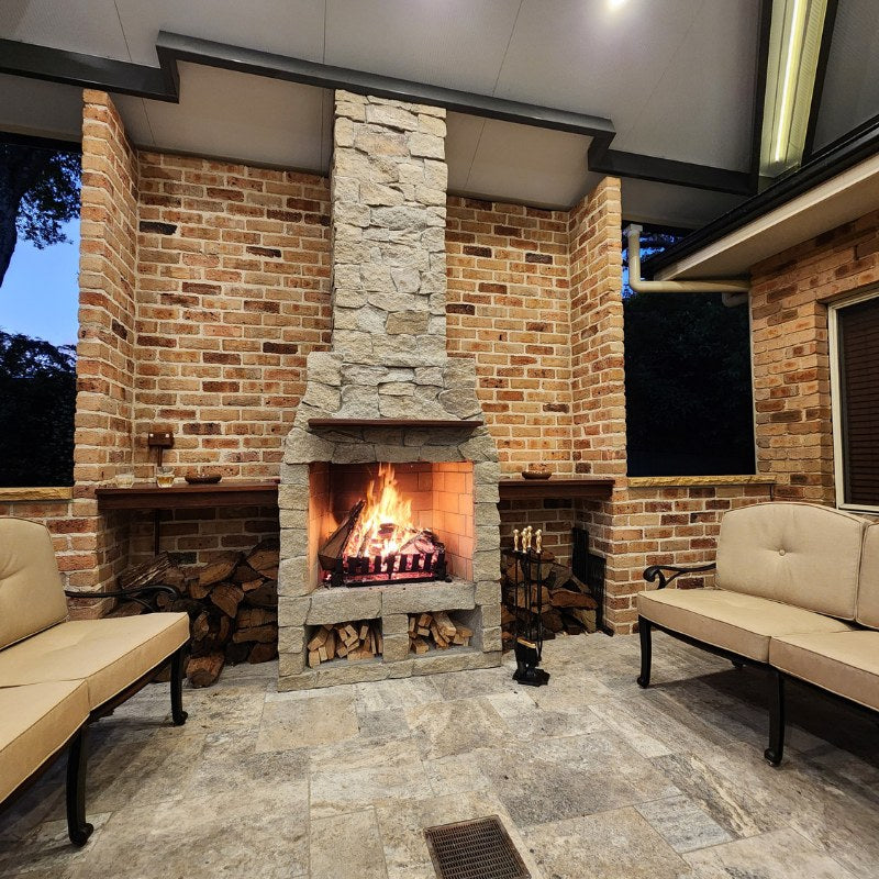 Ochre Living Hotham Complete Fireplace Kit at night beside a timber-clad house with outdoor lounge seating and a bright fire burning, showing an outdoor fireplace with chimney Australia in an evening setting.