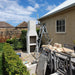 The Ochre Living Ossa Complete Fireplace Kit assembled outdoors before rendering, showing the fireplace structure and chimney during installation in an Australian backyard.