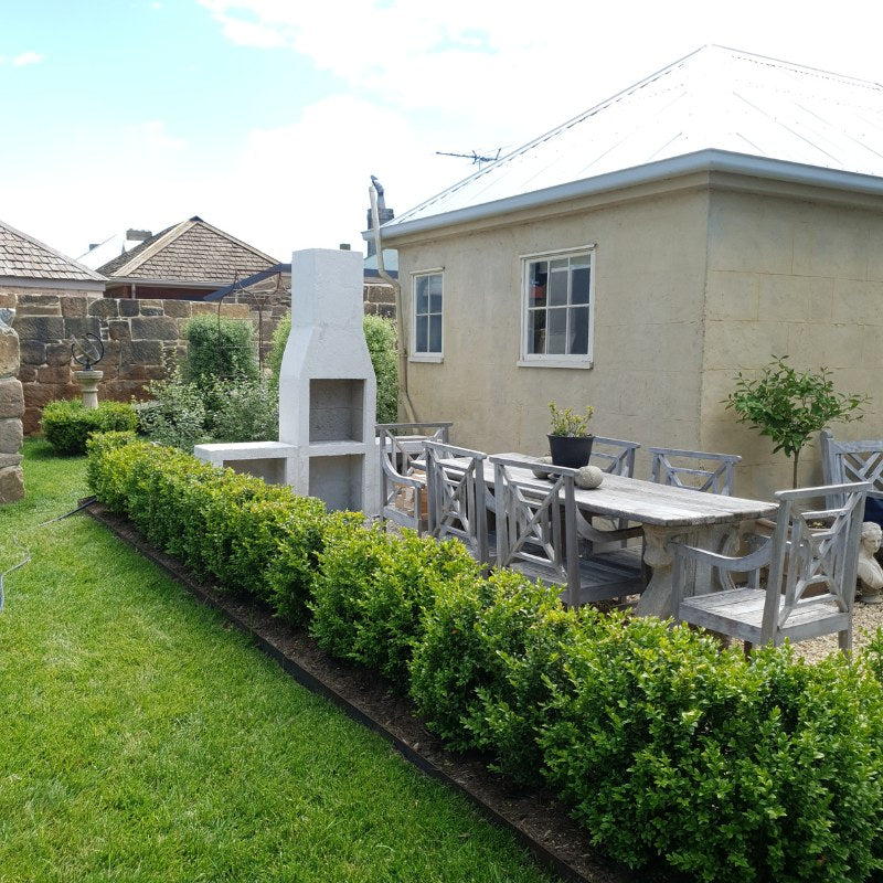 Completed rendered Ochre Living Ossa Complete Fireplace Kit in a garden setting before final firebrick fitting, showing the chimney fireplace and side storage benches.