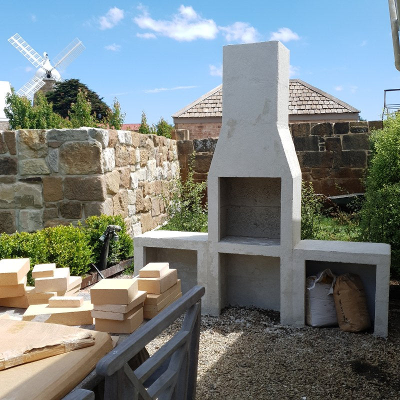Installer rendering the side bench section of the Ochre Living Ossa Complete Fireplace Kit during outdoor fireplace installation in a backyard setting.