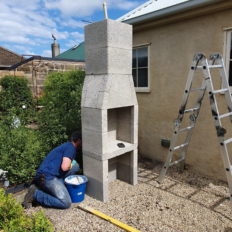 Fireplace components for the Ochre Living Ossa Complete Fireplace Kit laid out before assembly, including pumice blocks, firebricks, adhesive, and render materials for installation.