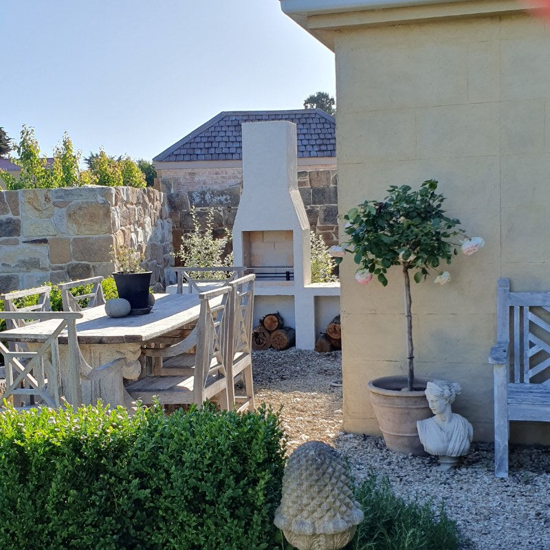 Front studio image of the Ochre Living Ossa Complete Fireplace Kit showing the main rendered outdoor fireplace with chimney and lower log storage opening on a plain background.