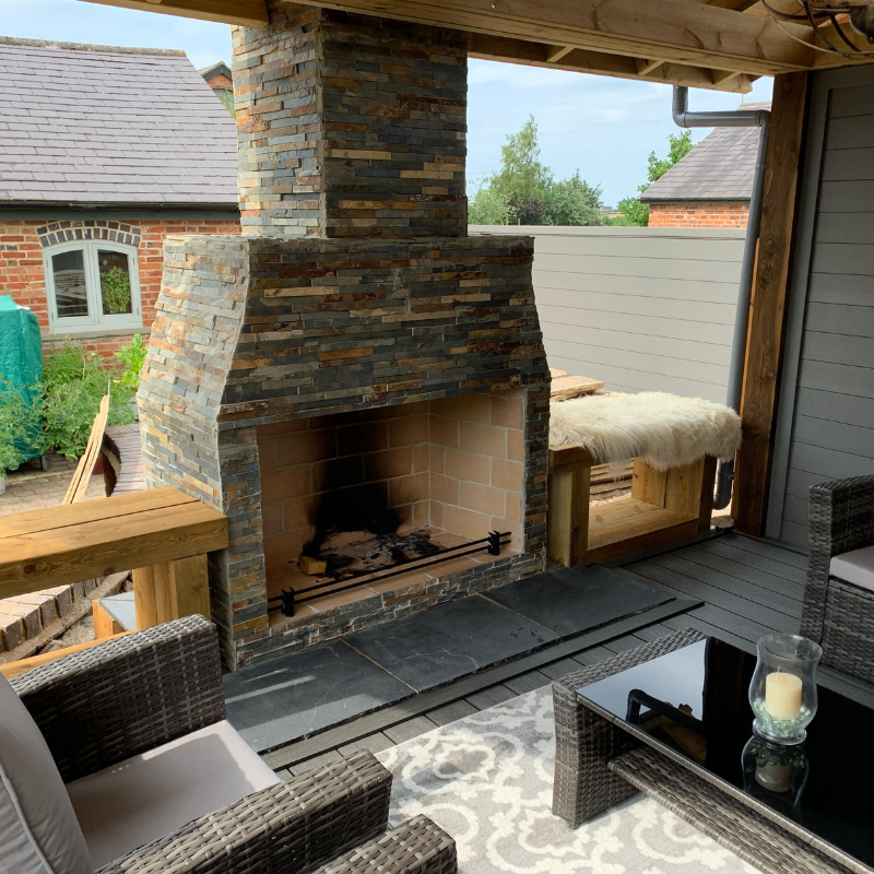 Installed Ochre Living Perisher Complete Fireplace Kit on a covered patio, finished in stacked stone and styled within an outdoor entertaining area with seating and timber beams