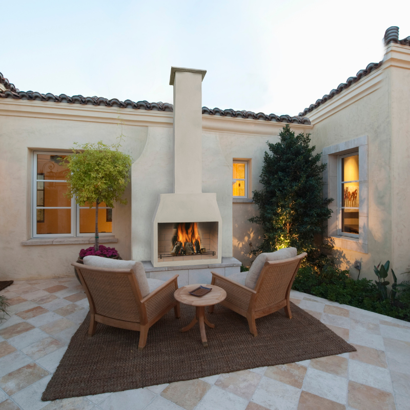 Ochre Living Perisher Complete Fireplace Kit installed in a Mediterranean-style courtyard, creating a warm outdoor focal point between two lounge chairs and a small table.