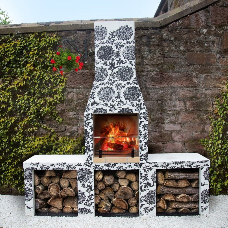 Decoratively finished Ochre Living Ossa Complete Fireplace Kit in a courtyard garden, styled with a black-and-white patterned surface and stacked firewood for outdoor fireplace inspiration in Australia.