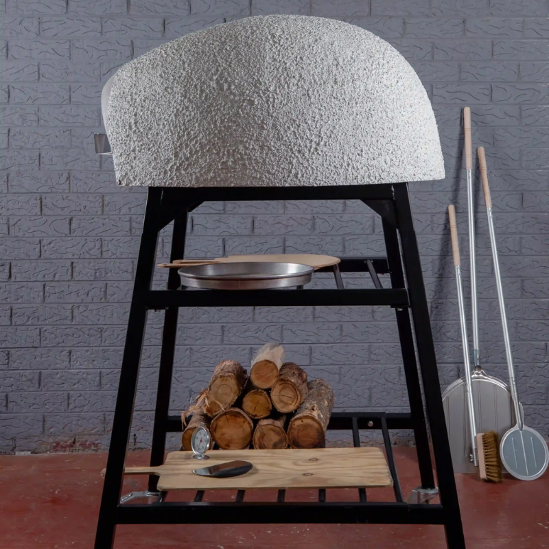 Rear view of the Polito Antonius Garden Wood Fired Oven highlighting the textured dome finish, black steel Polito pizza oven stand, firewood storage, and outdoor pizza accessories