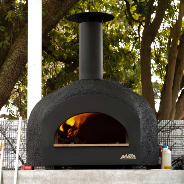 Polito Donatello II wood fire oven in black on metal feet, fire lit, sitting on a concrete outdoor bench