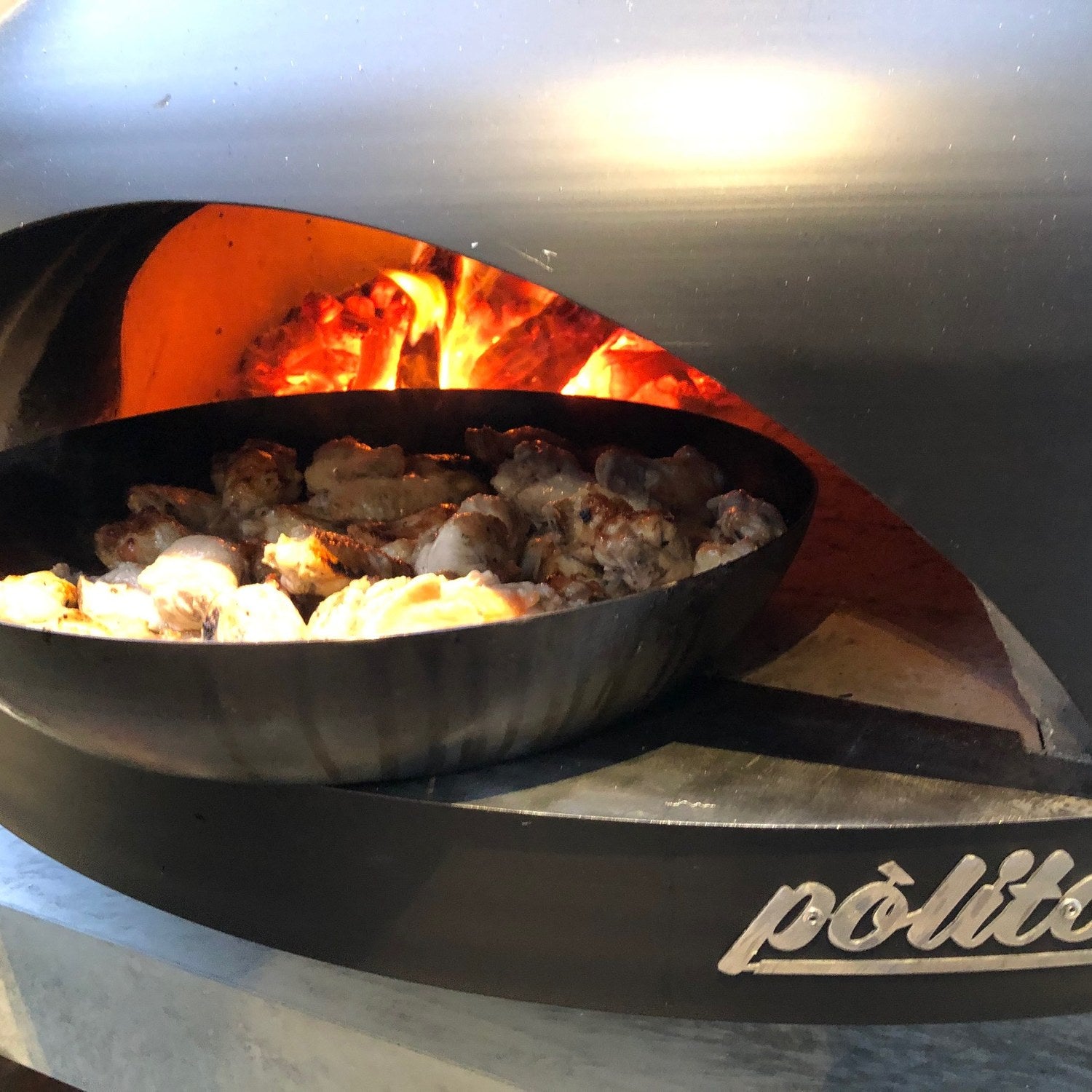 A pan of food cooking alongside the fire in a Polito Giotto