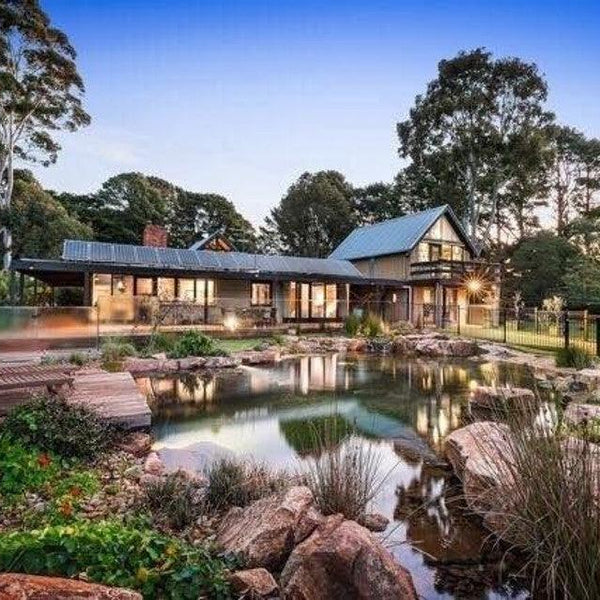 An Aquascape recreation pond beside an Australian home at dusk, with rock edging, a timber deck and planted wetland margins
