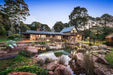 An Aquascape recreation pond beside an Australian home at dusk, with rock edging, a timber deck and planted wetland margins