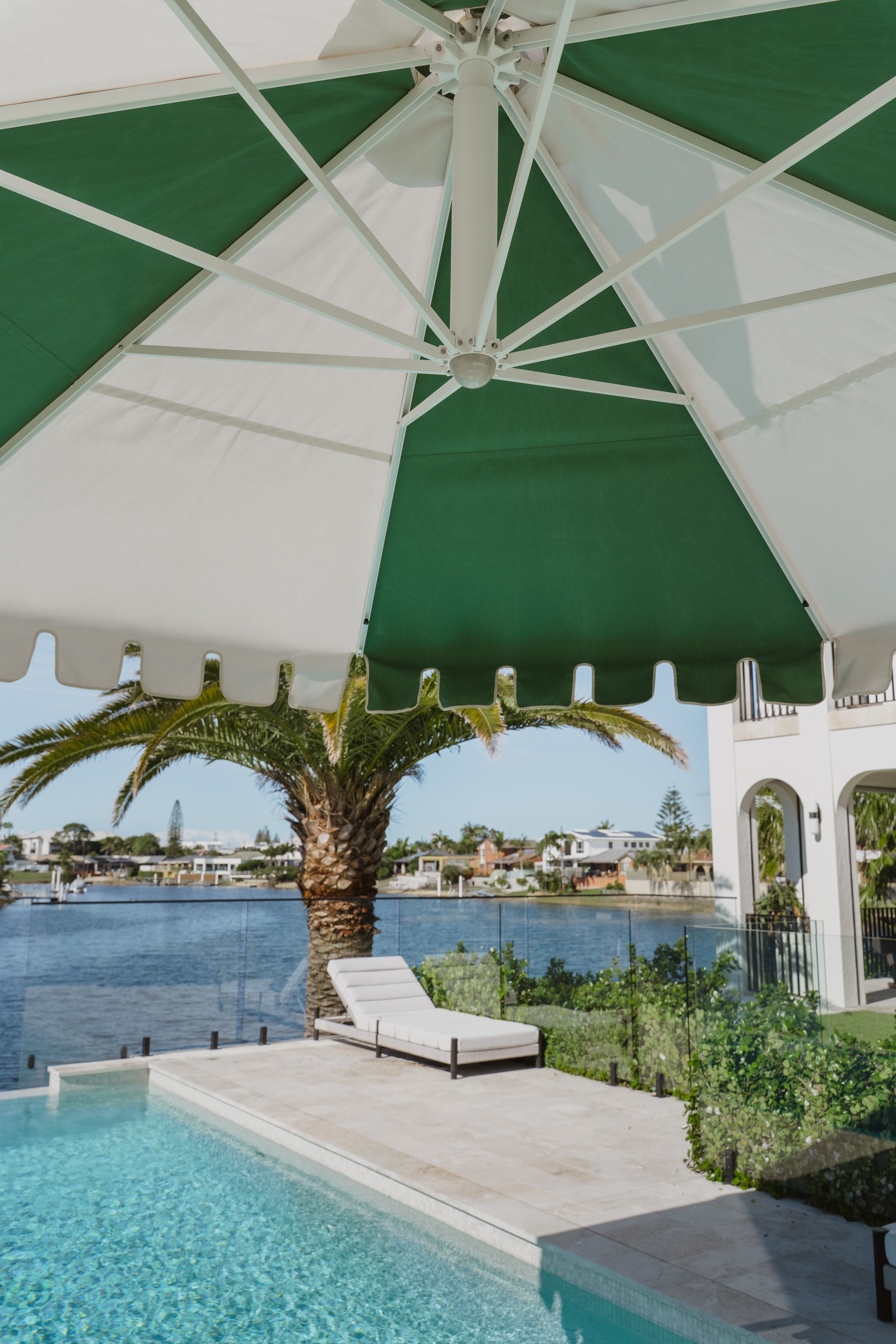 Revolvashade Designer Collection cantilever umbrella with a green and cream striped valance canopy shading an infinity pool courtyard