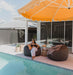 Revolvashade Designer Collection cantilever umbrella with an orange and white striped canopy over poolside seating