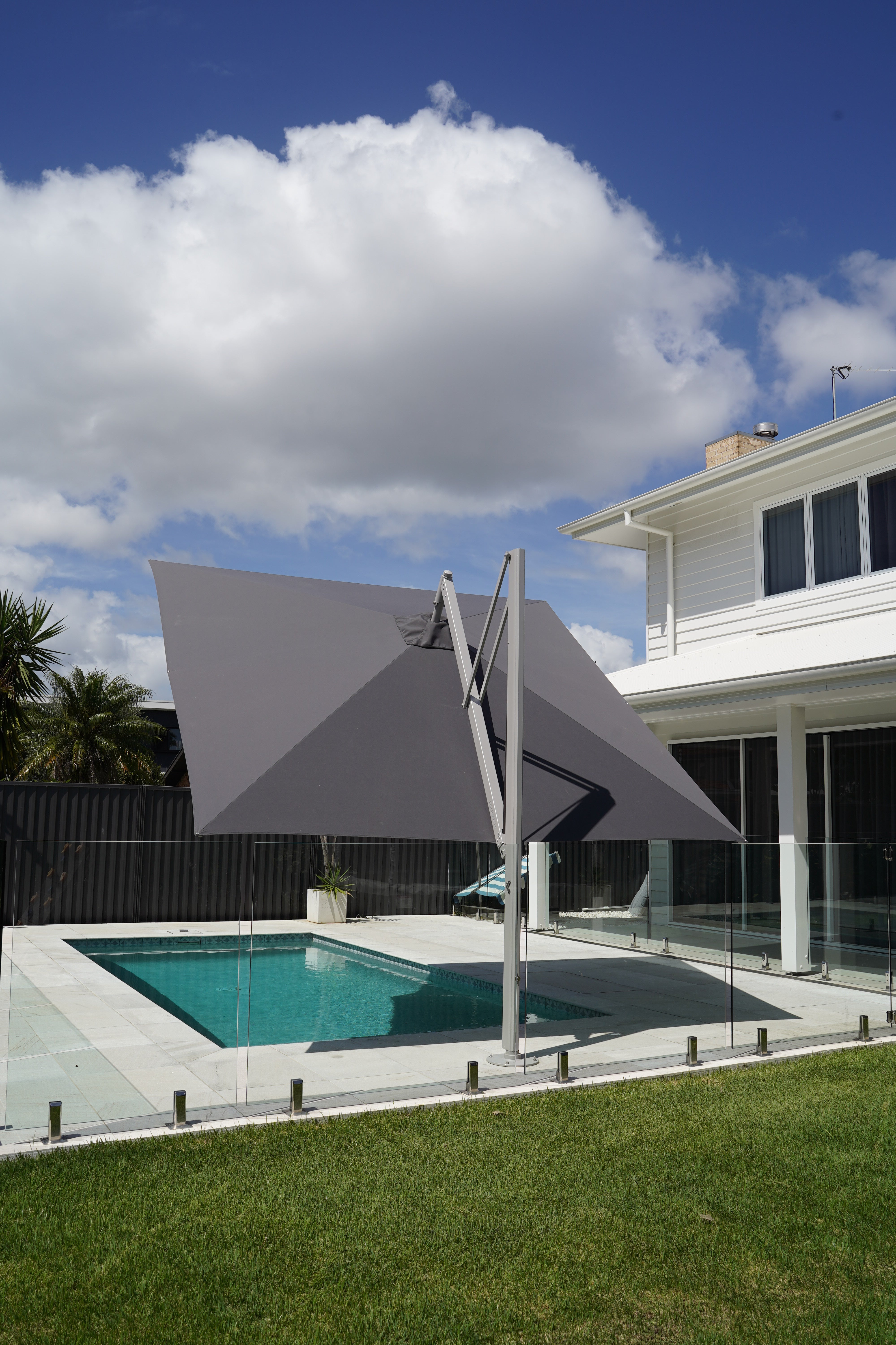 Revolvashade Signature Range cantilever umbrella with a charcoal canopy in the Square shape, tilted over a glass-fenced pool deck