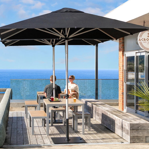 Shadowspec Oasis market umbrellas in black over cafe tables on a clifftop terrace