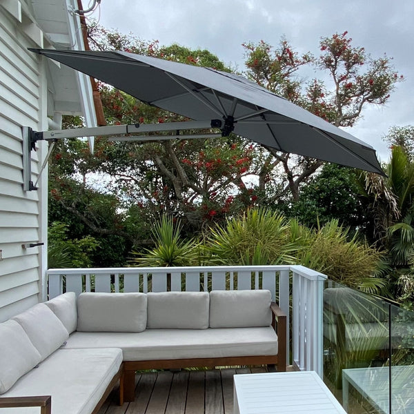 Shadowspec Retreat wall-mounted umbrella with a Charcoal Tweed canopy over a timber deck lounge