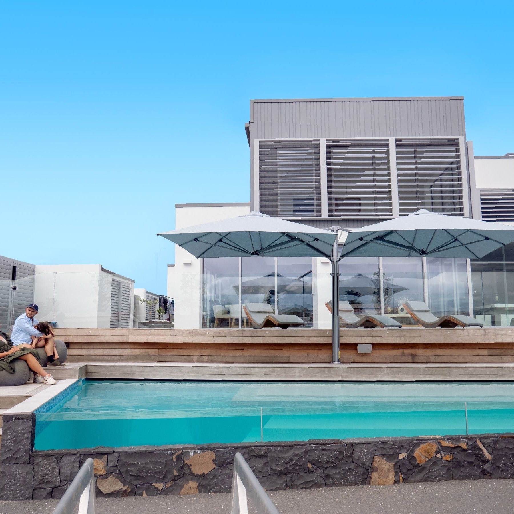 Shadowspec Unity twin-canopy cantilever umbrella in grey-blue over a pool