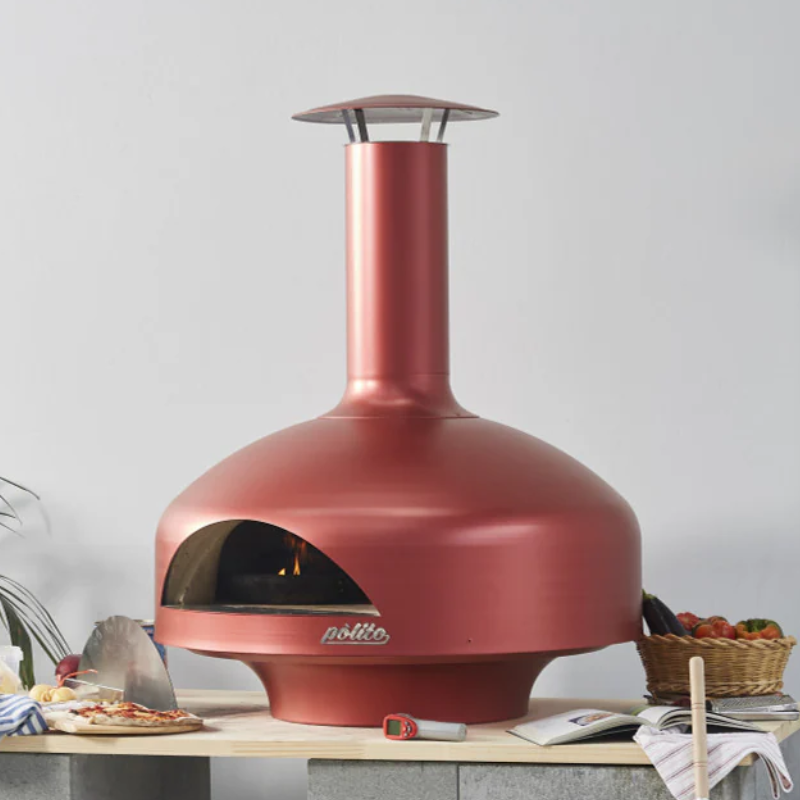 Shimmering Rose Polito Giotto Oven BTS freestanding outdoor pizza oven displayed on a stone bench with pizza making ingredients and accessories in a contemporary entertaining space