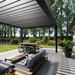 Black SkyFlex Delta motorised aluminium louvred pergola covering an outdoor lounge and dining patio beside water
