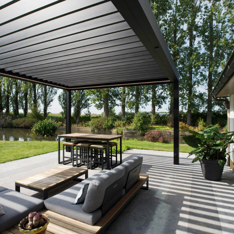 Black SkyFlex Delta motorised aluminium louvred pergola covering an outdoor lounge and dining patio beside water