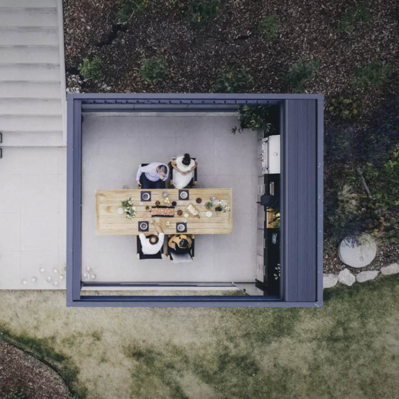 Top-down view of a black SkyFlex Delta Open Sky motorised aluminium louvred pergola covering an outdoor dining table beside a house