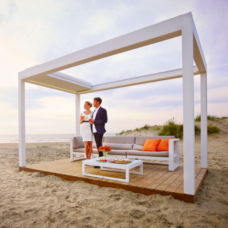 White SkyFlex Delta Open Sky motorised aluminium louvred pergola installed on a beachside platform with lounge seating and two people standing underneath