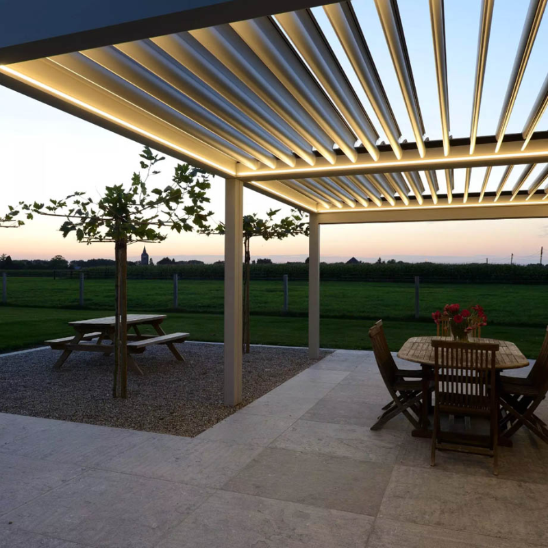 White SkyFlex Delta Open Sky motorised aluminium louvred pergola with integrated LED lighting above an outdoor dining patio at sunset