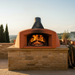 A luxury indoor installation of the Valoriani Family TOP100 Pizza Oven—shown with a live wood fire glowing inside the chamber, set against a modern stone-tiled splashback.
