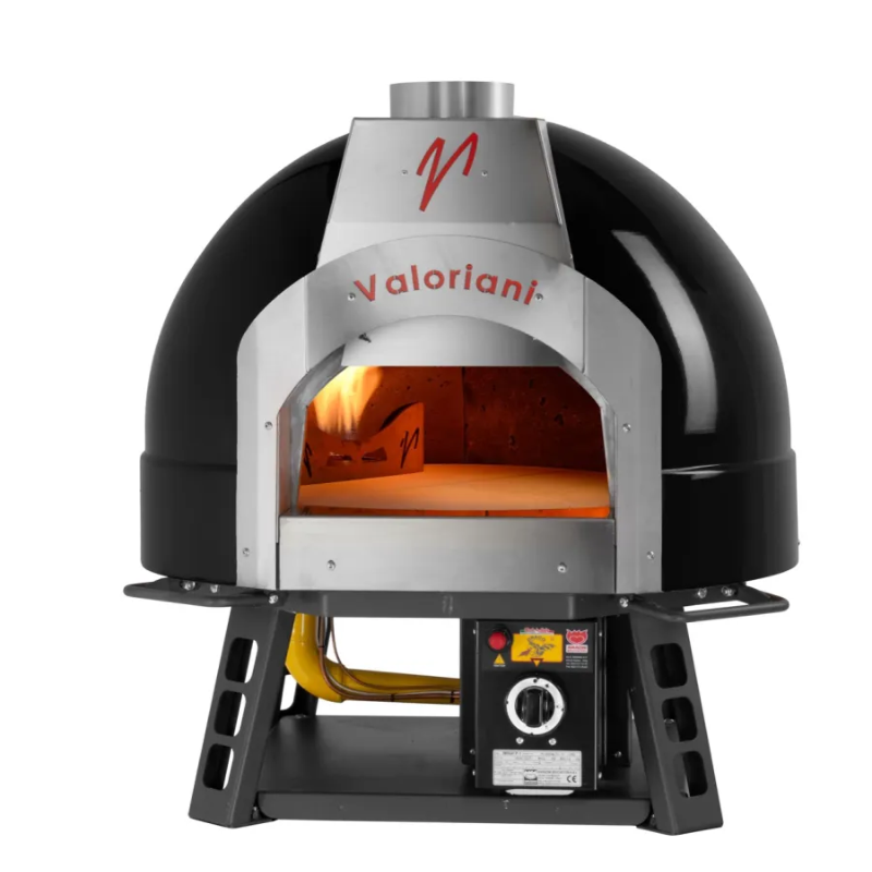 A studio shot against a white background featuring a black Valoriani Family BABY F75 Pizza Oven gas model. The oven is mounted on a low, heavy-duty black metal stand. Inside the stainless steel arched opening, a gas burner provides a steady flame that illuminates the stone cooking floor.