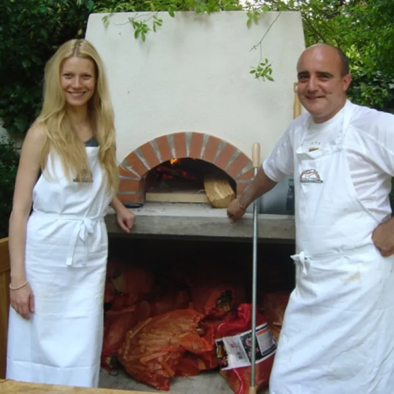 Lifestyle shot showing the elegant Valoriani pizza oven in a rustic outdoor kitchen setup