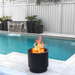 VisionLINE Fire Pit Mini V2 in black burning beside a swimming pool, with bright flames rising from the round fire pit near white outdoor tiles and garden planters.