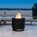 The VisionLINE Fire Pit V2 in use during the evening, with vibrant flames emanating from the center, set in a stylish outdoor seating area with modern furniture.
