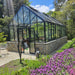 Winter Gardenz Elite 10ft wide glasshouse with black aluminium frame on a stone base wall in a landscaped garden